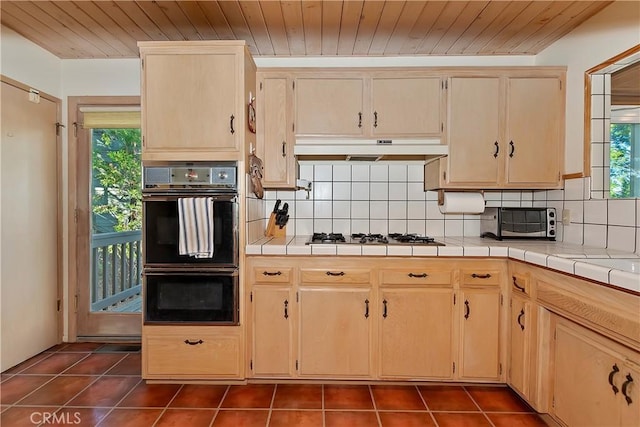 kitchen with backsplash, wood ceiling, stainless steel gas stovetop, double oven, and tile counters