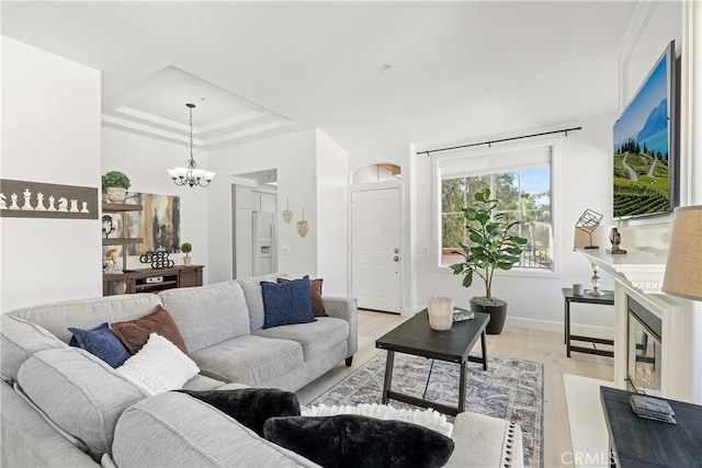 living room with a chandelier, a tray ceiling, and light hardwood / wood-style flooring