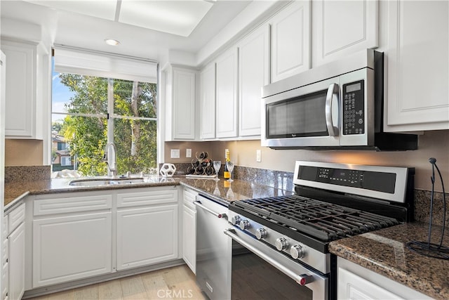 kitchen with white cabinetry, sink, stainless steel appliances, dark stone countertops, and light wood-type flooring