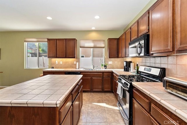 kitchen featuring a center island, tile counters, stainless steel appliances, sink, and light tile patterned flooring