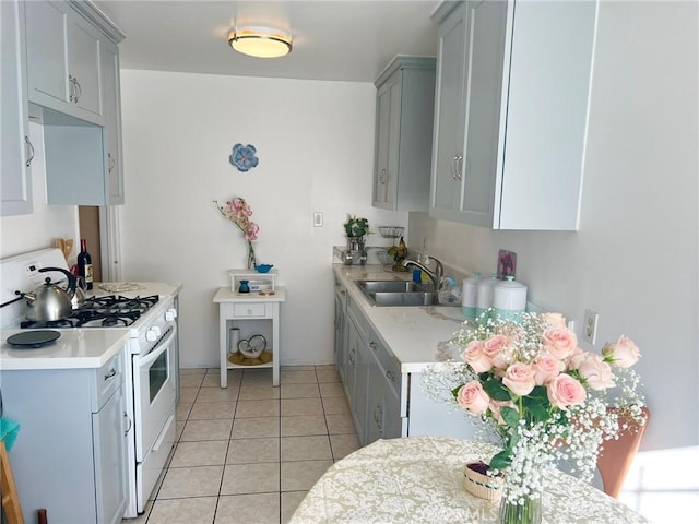 kitchen featuring gray cabinets, sink, light tile patterned floors, and white range with gas stovetop