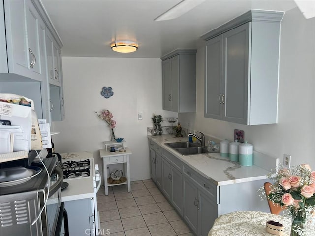 kitchen featuring light tile patterned floors, white gas range oven, gray cabinetry, and sink