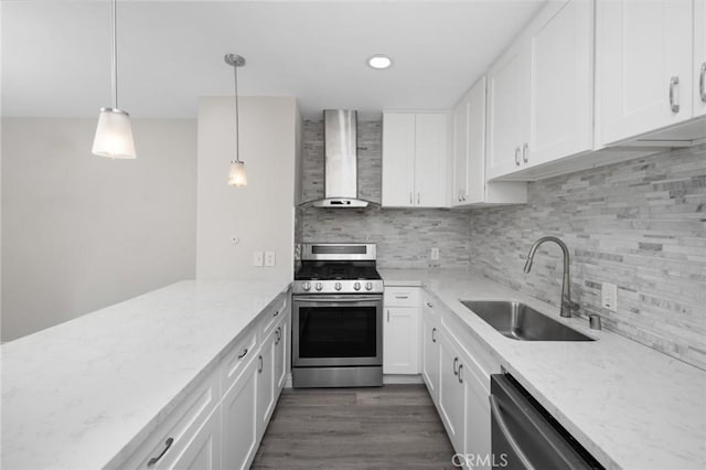 kitchen with pendant lighting, sink, wall chimney exhaust hood, appliances with stainless steel finishes, and white cabinetry