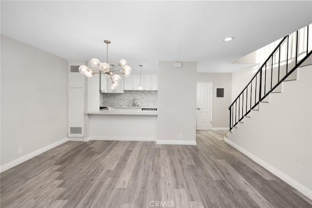 unfurnished living room with light hardwood / wood-style floors, an inviting chandelier, and sink