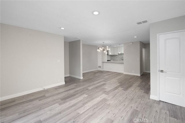 unfurnished living room with an inviting chandelier and light hardwood / wood-style flooring