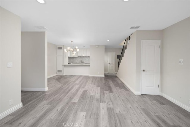 unfurnished living room featuring light wood-type flooring and an inviting chandelier