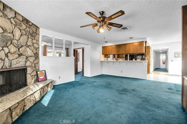 unfurnished living room featuring a textured ceiling, ceiling fan, dark carpet, and a fireplace