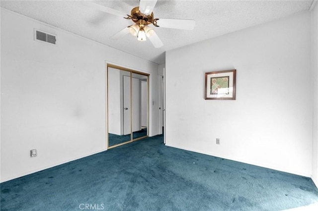 empty room featuring ceiling fan, dark carpet, and a textured ceiling