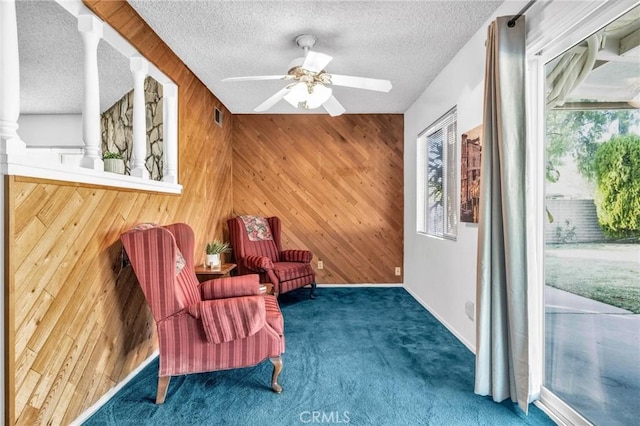 living area with carpet, wood walls, ceiling fan, and a textured ceiling