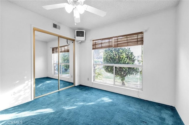 unfurnished bedroom featuring ceiling fan, dark carpet, a textured ceiling, and a closet