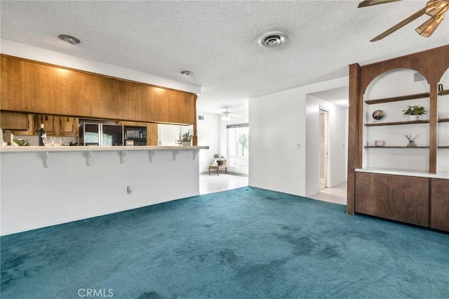 unfurnished living room with a textured ceiling, light colored carpet, and ceiling fan