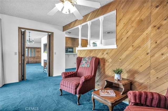 sitting room featuring carpet flooring, wooden walls, ceiling fan with notable chandelier, and a textured ceiling