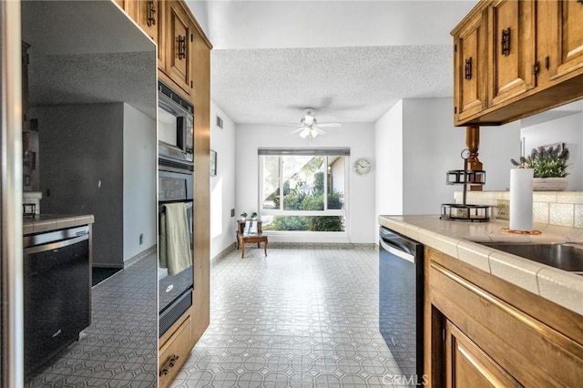 kitchen featuring tile countertops, ceiling fan, stainless steel appliances, and a textured ceiling