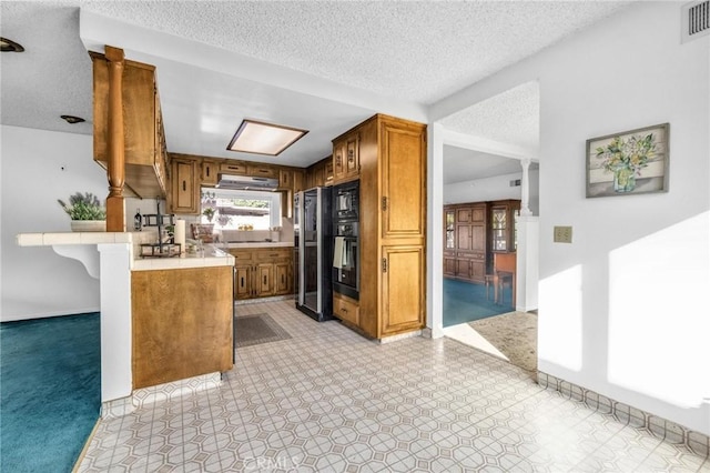 kitchen featuring ornate columns, kitchen peninsula, a textured ceiling, a kitchen bar, and black appliances