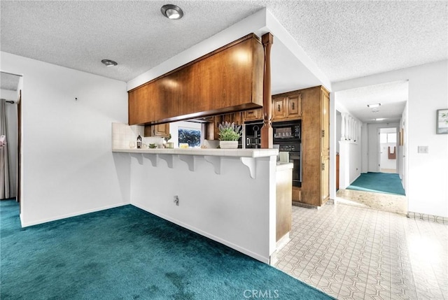 kitchen with a kitchen breakfast bar, kitchen peninsula, black appliances, and a textured ceiling