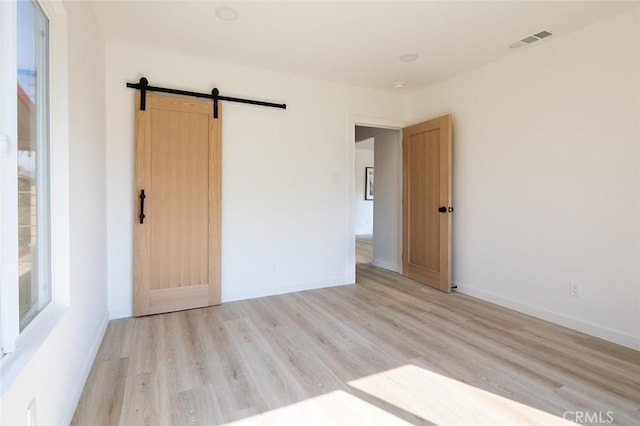 unfurnished room with a barn door and light hardwood / wood-style flooring