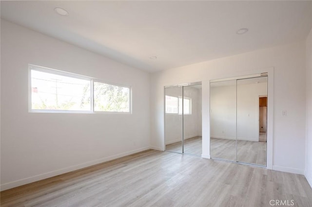 unfurnished bedroom featuring light hardwood / wood-style floors, multiple closets, and multiple windows