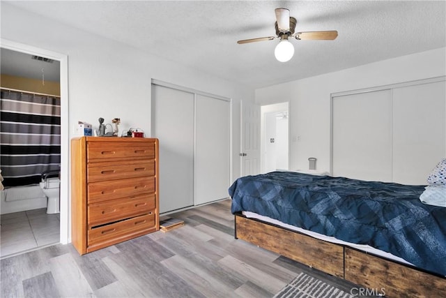 bedroom with two closets, ceiling fan, light hardwood / wood-style flooring, and a textured ceiling