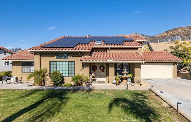 mediterranean / spanish home featuring solar panels, a mountain view, a front lawn, and a garage