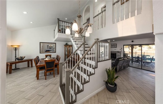 stairs featuring a fireplace, wood-type flooring, a high ceiling, and a notable chandelier