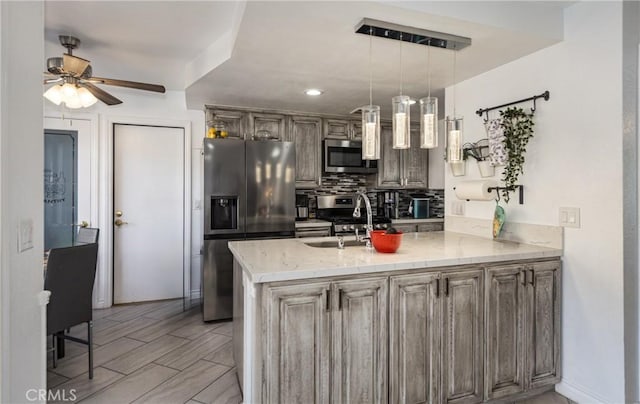 kitchen with kitchen peninsula, appliances with stainless steel finishes, ceiling fan, sink, and pendant lighting