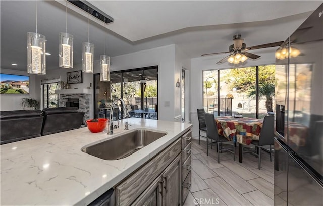 kitchen with light stone countertops, ceiling fan, sink, pendant lighting, and a fireplace