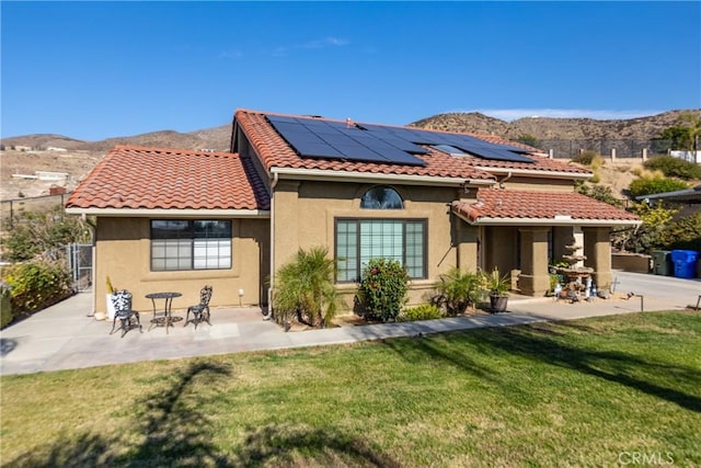 rear view of property with a mountain view, solar panels, a patio, and a lawn