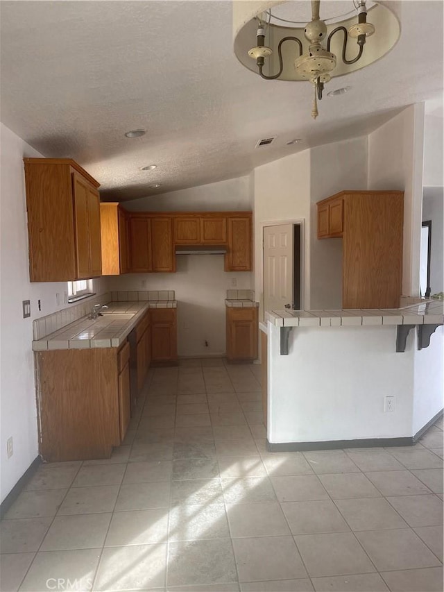 kitchen with vaulted ceiling, tile countertops, sink, a kitchen breakfast bar, and kitchen peninsula