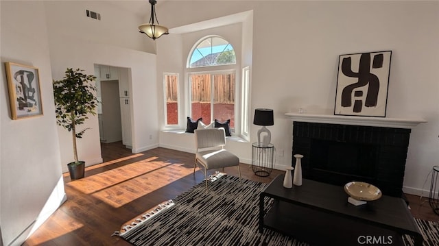 living room featuring a towering ceiling, wood-type flooring, and a brick fireplace