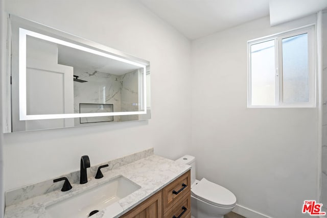 bathroom with a tile shower, vanity, and toilet