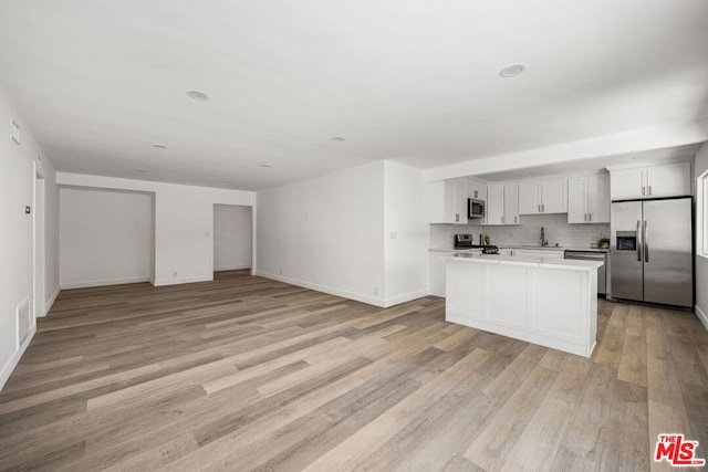 kitchen featuring white cabinetry, a center island, stainless steel appliances, decorative backsplash, and light wood-type flooring