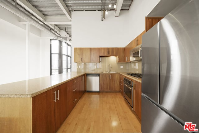 kitchen featuring kitchen peninsula, stainless steel appliances, backsplash, light wood-type flooring, and sink