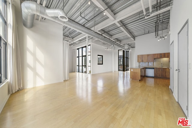 unfurnished living room featuring light wood-type flooring, a towering ceiling, and sink