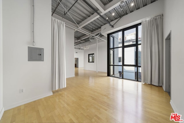 unfurnished room with light wood-type flooring, electric panel, beam ceiling, and a towering ceiling