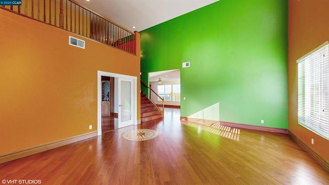 unfurnished living room featuring hardwood / wood-style floors, ceiling fan, a towering ceiling, and french doors