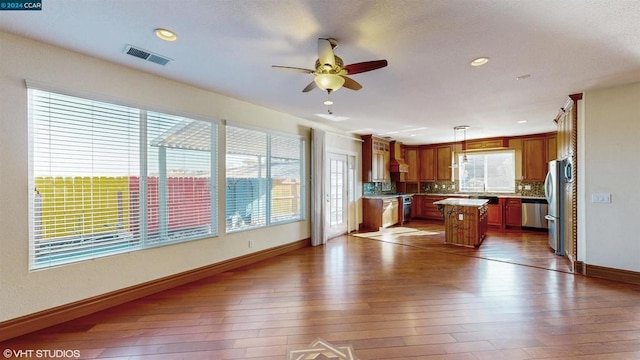 kitchen featuring appliances with stainless steel finishes, ceiling fan, dark wood-type flooring, decorative light fixtures, and a kitchen island