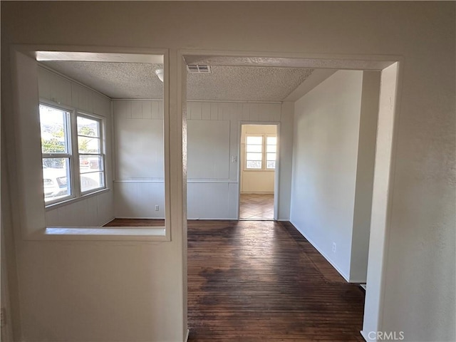 corridor with a wealth of natural light, dark hardwood / wood-style flooring, and a textured ceiling