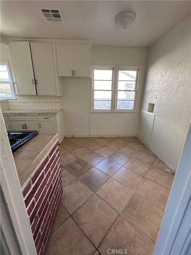 kitchen with tasteful backsplash, white cabinetry, and light tile patterned flooring