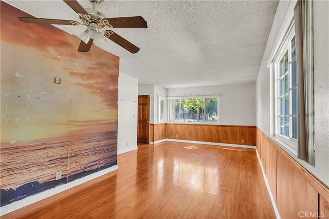 unfurnished room with ceiling fan, wooden walls, a textured ceiling, and light wood-type flooring