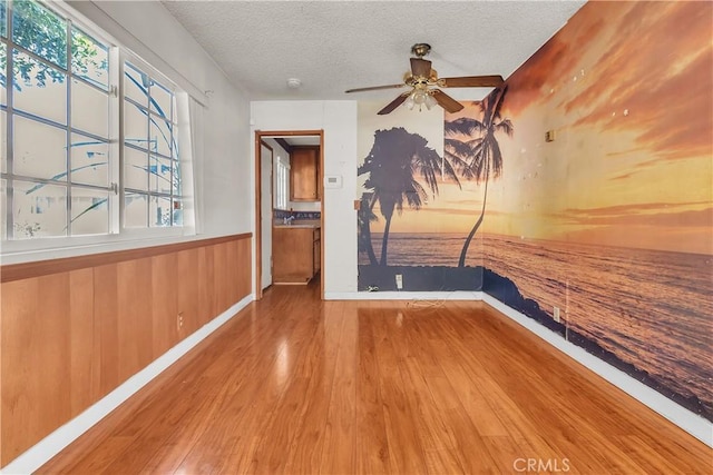 empty room with wooden walls, hardwood / wood-style floors, ceiling fan, and a textured ceiling