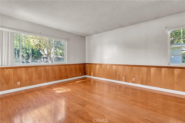 spare room with a textured ceiling, hardwood / wood-style flooring, and a healthy amount of sunlight