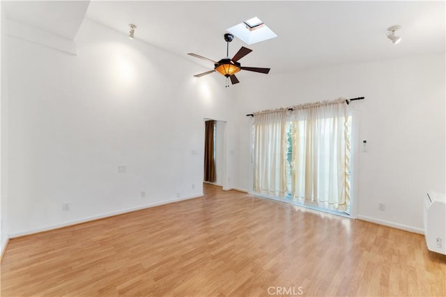 empty room with ceiling fan, light hardwood / wood-style floors, high vaulted ceiling, and a skylight