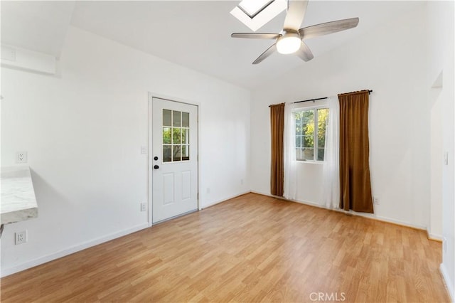 spare room featuring vaulted ceiling with skylight, ceiling fan, and light hardwood / wood-style flooring