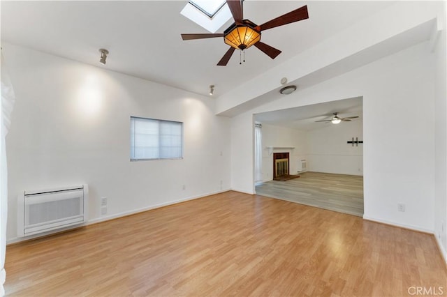 unfurnished living room with vaulted ceiling with skylight, ceiling fan, and light hardwood / wood-style flooring