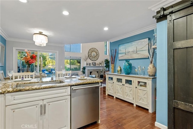 kitchen with stainless steel dishwasher, light stone counters, crown molding, a barn door, and white cabinetry