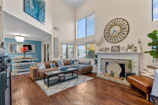 living room featuring a stone fireplace, a notable chandelier, crown molding, a towering ceiling, and hardwood / wood-style flooring