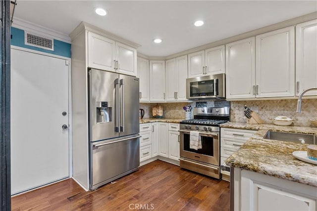 kitchen featuring appliances with stainless steel finishes, sink, white cabinets, dark hardwood / wood-style flooring, and light stone counters