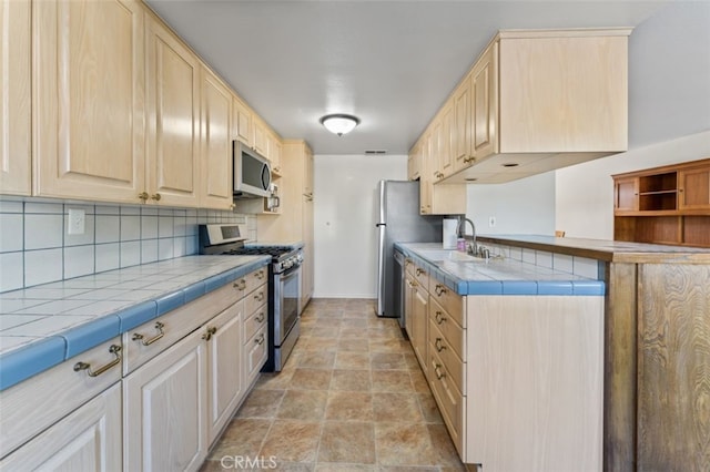 kitchen featuring light brown cabinets, sink, decorative backsplash, appliances with stainless steel finishes, and tile counters