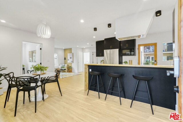 kitchen with a kitchen breakfast bar, stainless steel fridge, light hardwood / wood-style floors, and kitchen peninsula