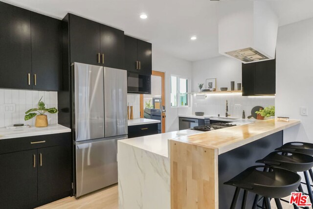 kitchen featuring decorative backsplash, appliances with stainless steel finishes, kitchen peninsula, a breakfast bar, and light hardwood / wood-style floors